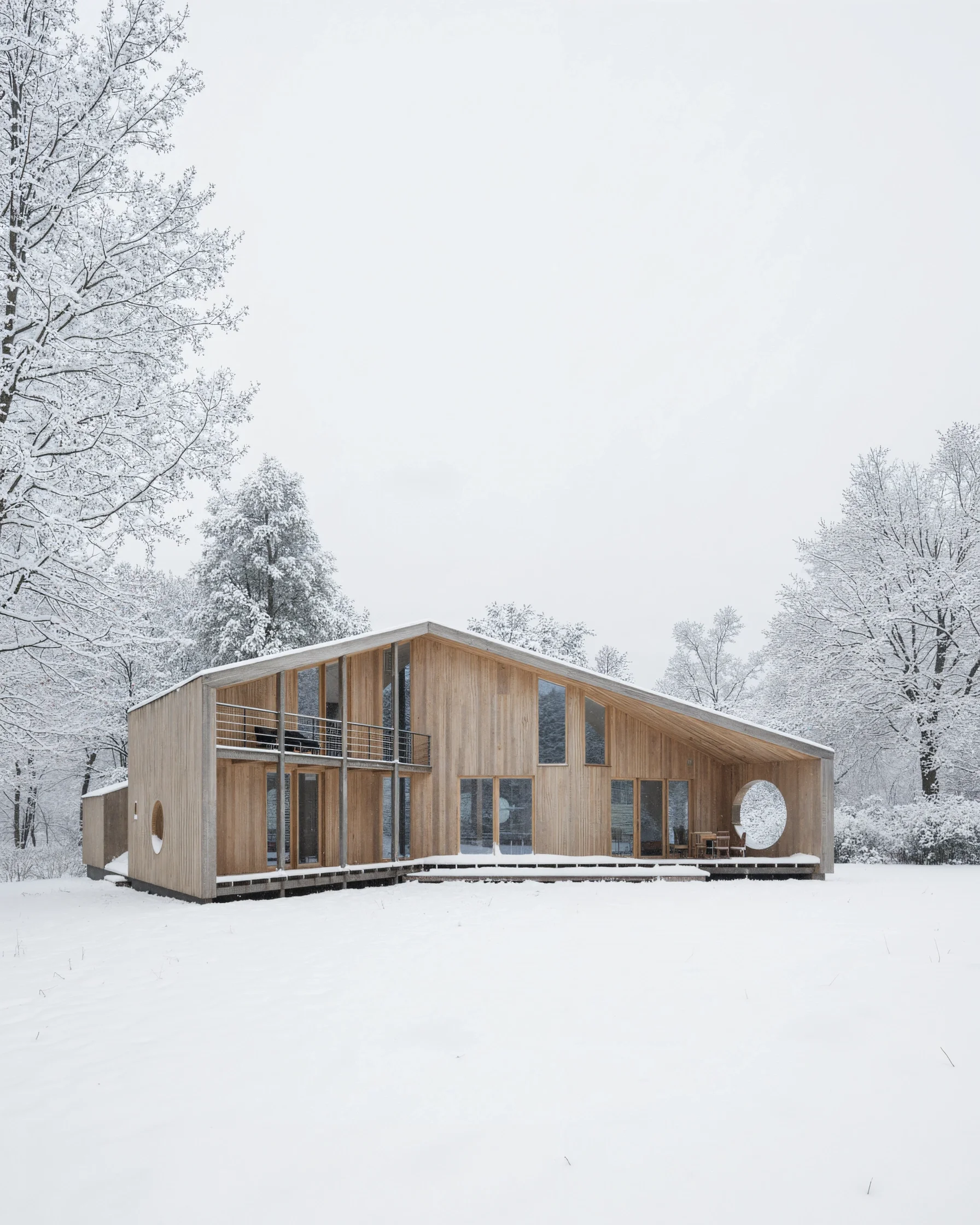 The Wing House in deep snow, its pale timber facade and round window against frosted trees.